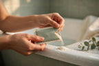 Hands tearing open a bath soak sachet over a bathtub