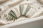 Bath soak sachets fanned out on linen beside a bathtub